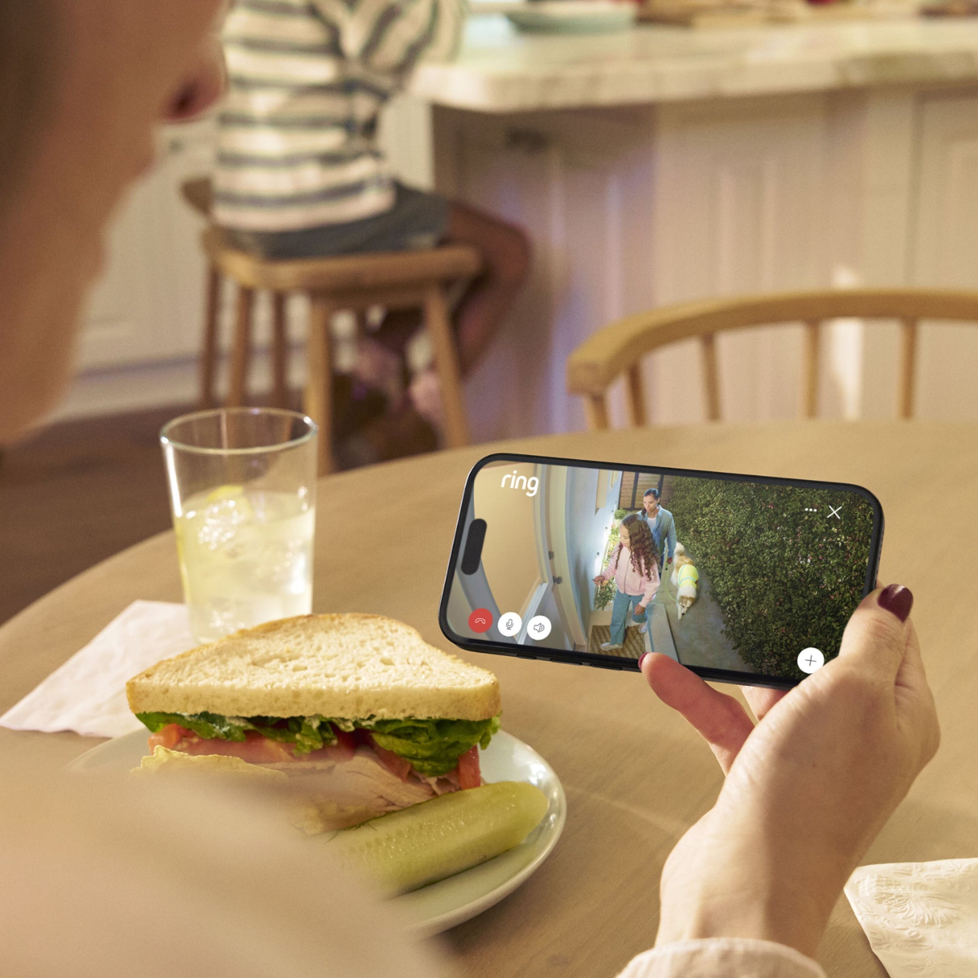 Ring Outdoor Cam Plus Plug-in Sort vises i app, 1080p Full HD live-feed af person ved dør samt borddetaljer i baggrunden.