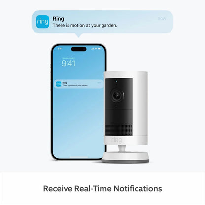Ring Outdoor Cam Plus Plug-in Hvid ved siden af smartphone med "Der er bevægelse i din have"-notifikation.