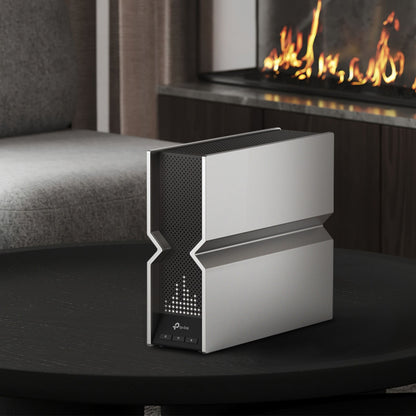 TP-Link Archer BE800 trådløs router Wifi 6 BE19000 sort, set fra siden på sort rundt bord, sofa og pejs i baggrunden.