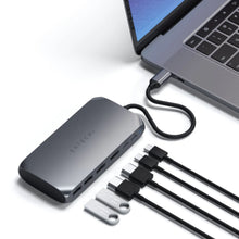Satechi M1 USB-C Multiadapter tilsluttet laptop, flere USB-C kabler og to flashdrev ved siden af, sølvfarvet.