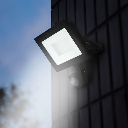 LED-projektør med bevægelsessensor 30 W 3380 lm monteret på mørk flisevæg oplyser område ved skumring.