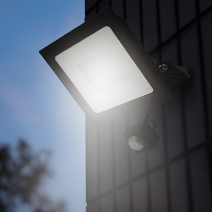 Luxorparts LED-projektør med bevægelsessensor 50 W 5750 lm monteret på mørk flisevæg til udendørs belysning.