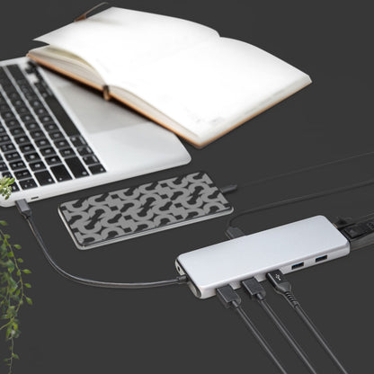 Sølvfarvet laptop tilsluttet Plexgear USB-C multiadapter 13 porte 100W, eksternt mønstret harddisk, flere kabler, åben notesbog.