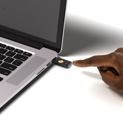 Yubico Sikkerhedsnøgle NFC med USB-A i laptop USB-port, hånd peger på nøgle, FIDO2 hardwarebaseret autentificering.