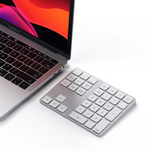 MacBook Pro sølv ved siden af Satechi Trådløs Numpad Sølv med hvide taster, laptopskærm i rød og sort.