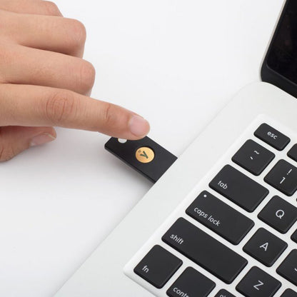 Yubico YubiKey 5 NFC Sikkerhedsnøgle USB-A i sort med guld cirkel, isat laptop nær tastatur, tofaktorautentificering.