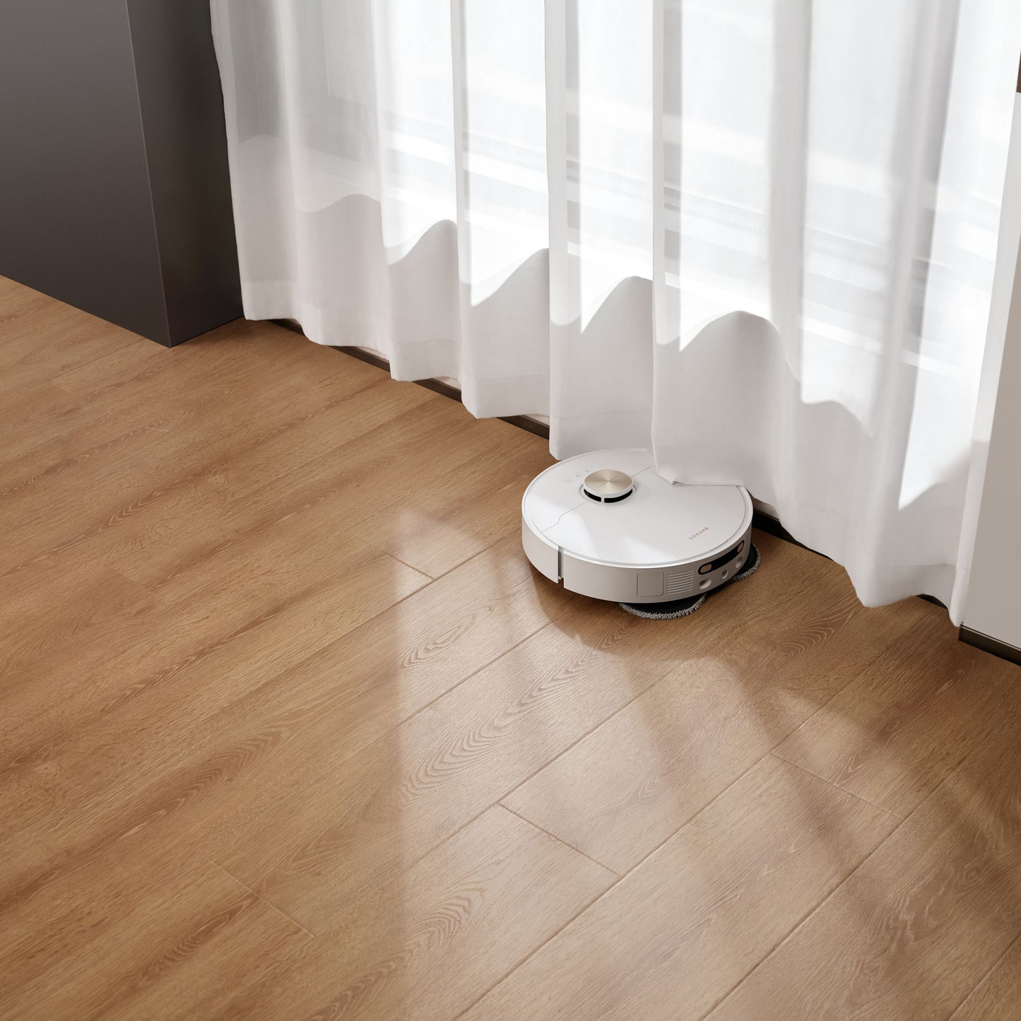 Dreame X40 Ultra fuldautomatisk støvsugerrobot på trægulv nær vindue med hvide gardiner, sollys i baggrunden.