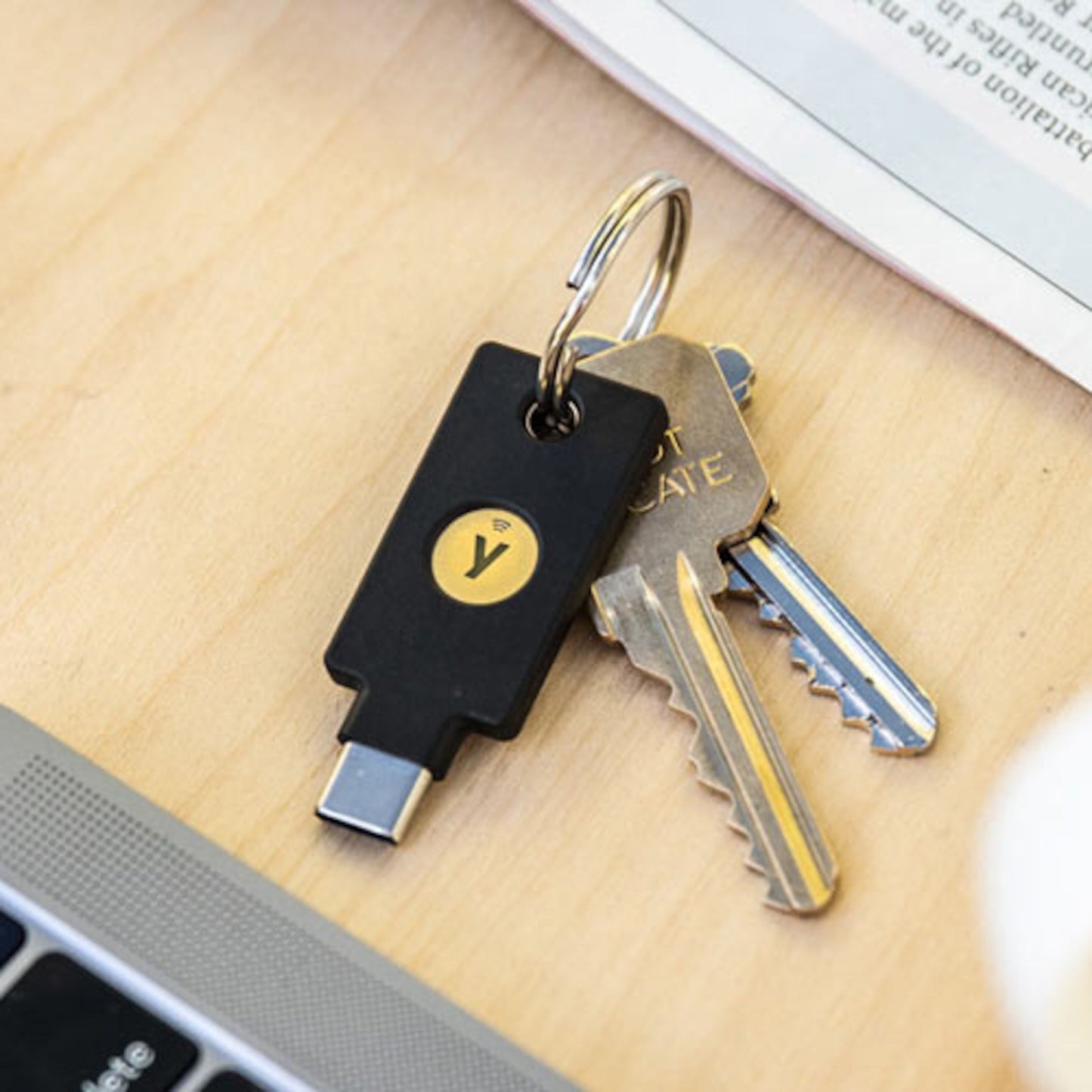 YubiKey 5C NFC USB-C sikkerhedsnøgle med gult Y-logo på nøglering sammen med to sølvfarvede husnøgler.