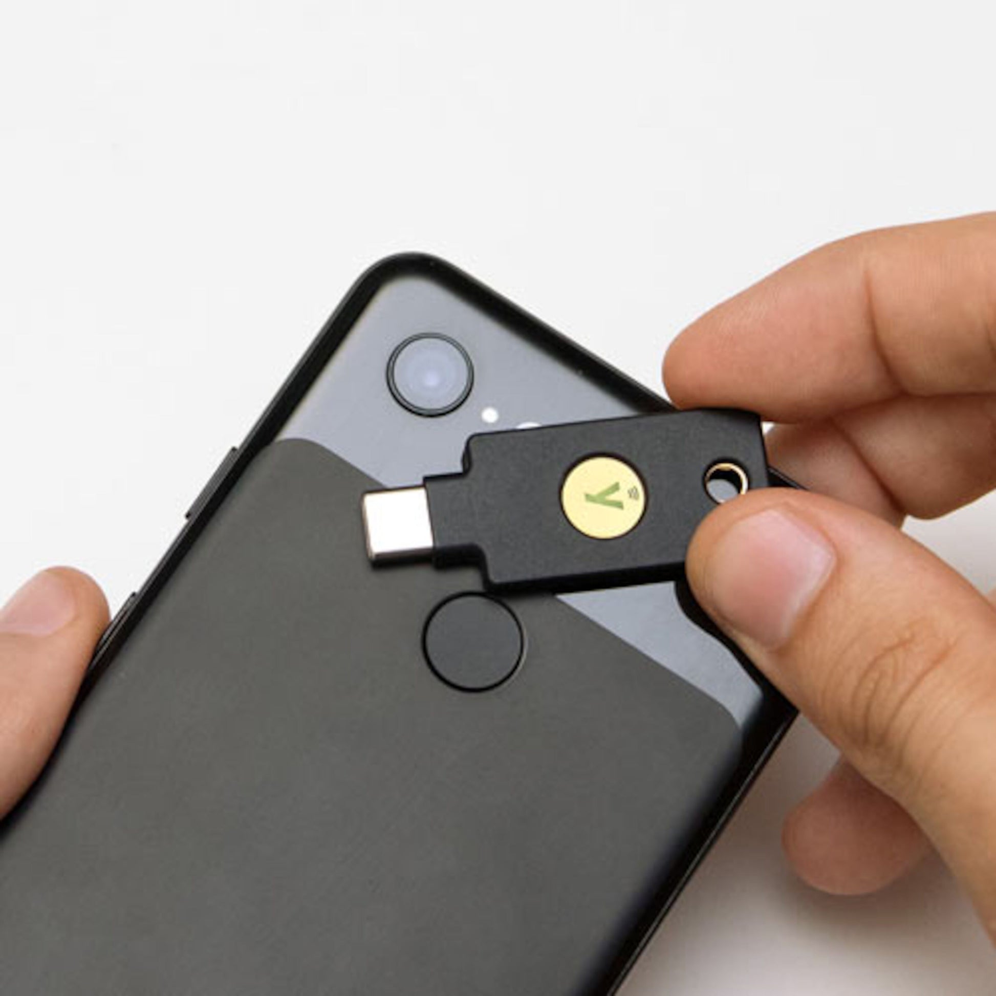 Yubico YubiKey 5C NFC sikkerhedsnøgle USB-C vises tæt på sort smartphone med synlige fingeraftrykslæser og kamera.