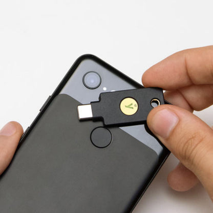 Yubico YubiKey 5C NFC sikkerhedsnøgle USB-C vises tæt på sort smartphone med synlige fingeraftrykslæser og kamera.