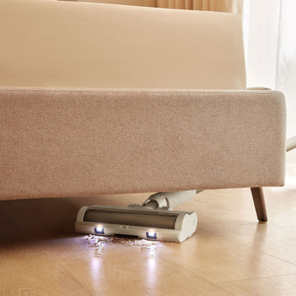 Dreame R10 støvsuger med LED-lys under beige sofa, opsamler snavs på lyst trægulv.