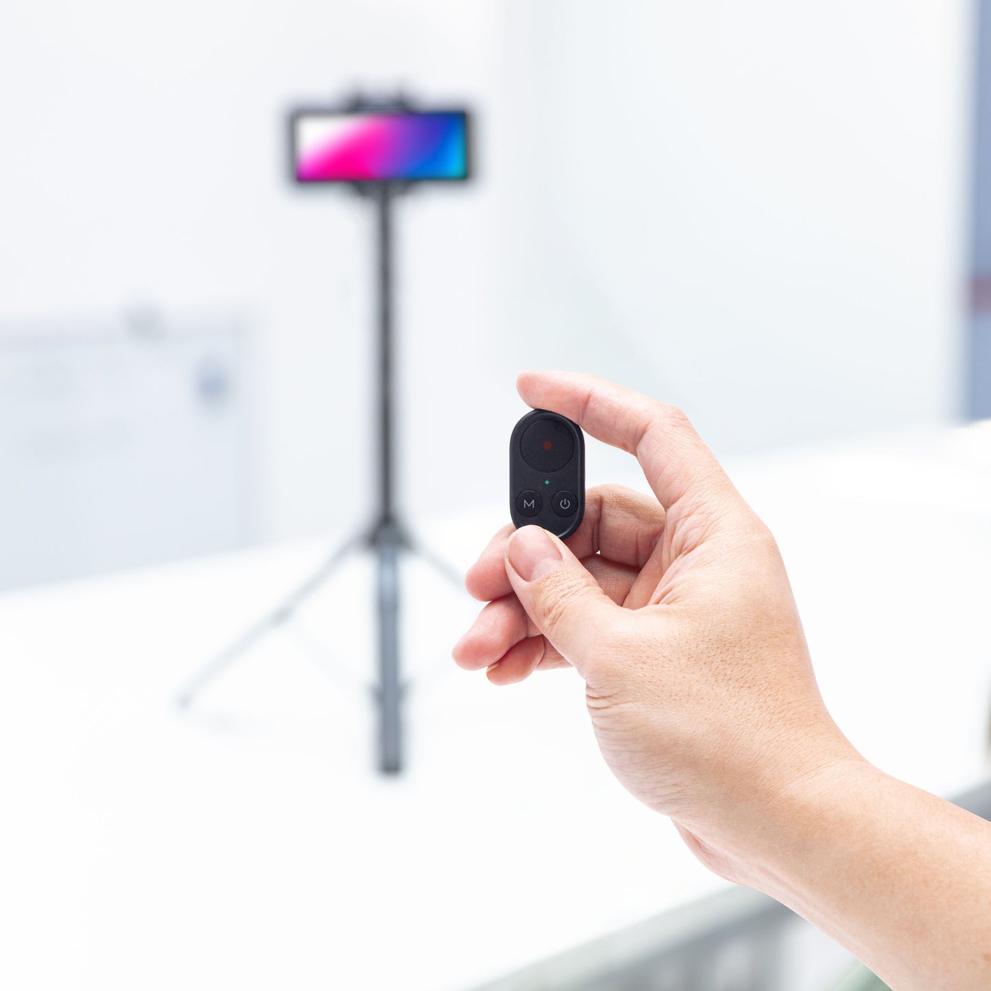Linocell Bluetooth fjernbetjening sort med én knap, smartphone på stativ sløret i baggrunden, Selfiestang med gimbal gen. 2.