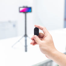 Linocell Bluetooth fjernbetjening sort med én knap, smartphone på stativ sløret i baggrunden, Selfiestang med gimbal gen. 2.