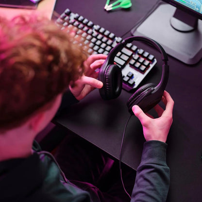 Trust GXT415 Zirox gaming-headset i hånd ved tastatur og skærm, synlig pink belysning.