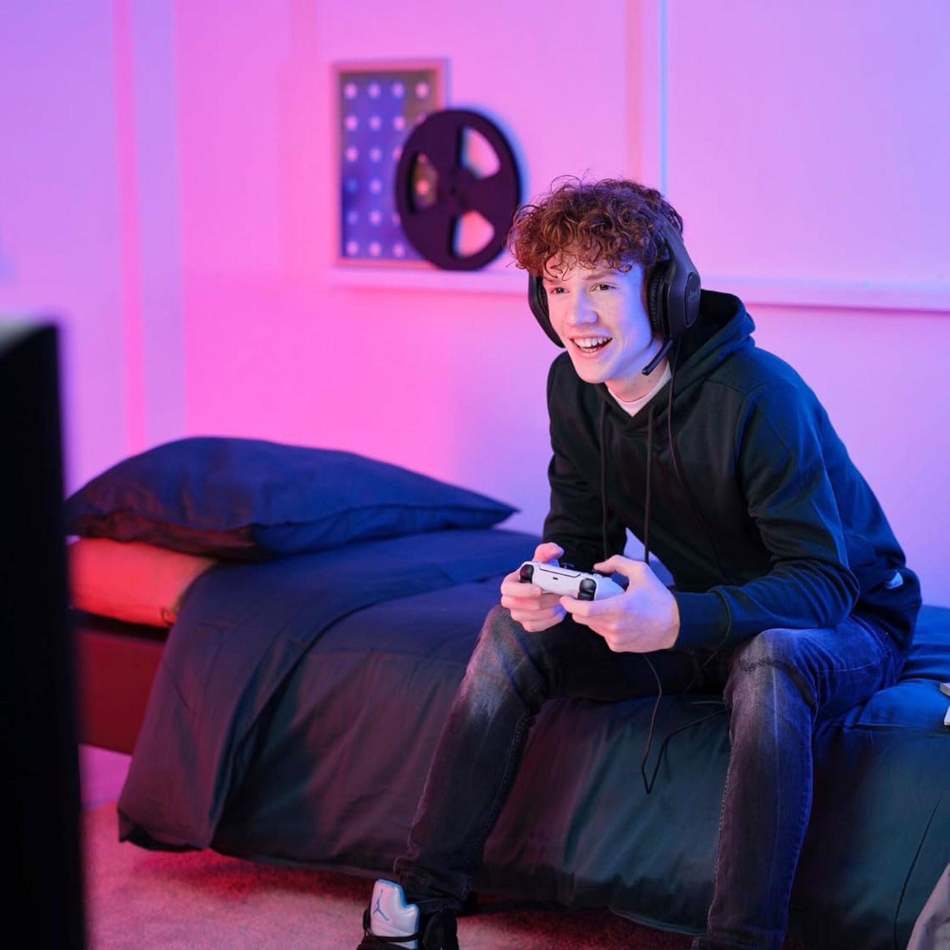 Trust GXT415 Zirox Gaming-headset sort bæres af ung person, sorte krøller, synlig mikrofon, pink/lilla belysning.