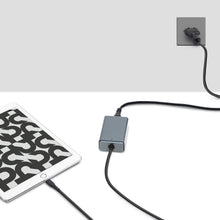 Tablet tilsluttet med sort kabel til Plexgear kompakt USB-C Computer oplader 65 W i stikkontakt, oplades.