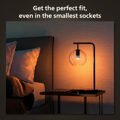Philips Hue Luster Kuglelampe White Ambiance E14 470 lm 2-pak på sengebord ved hvide puder, tekst: Passer perfekt til enhver fatning.