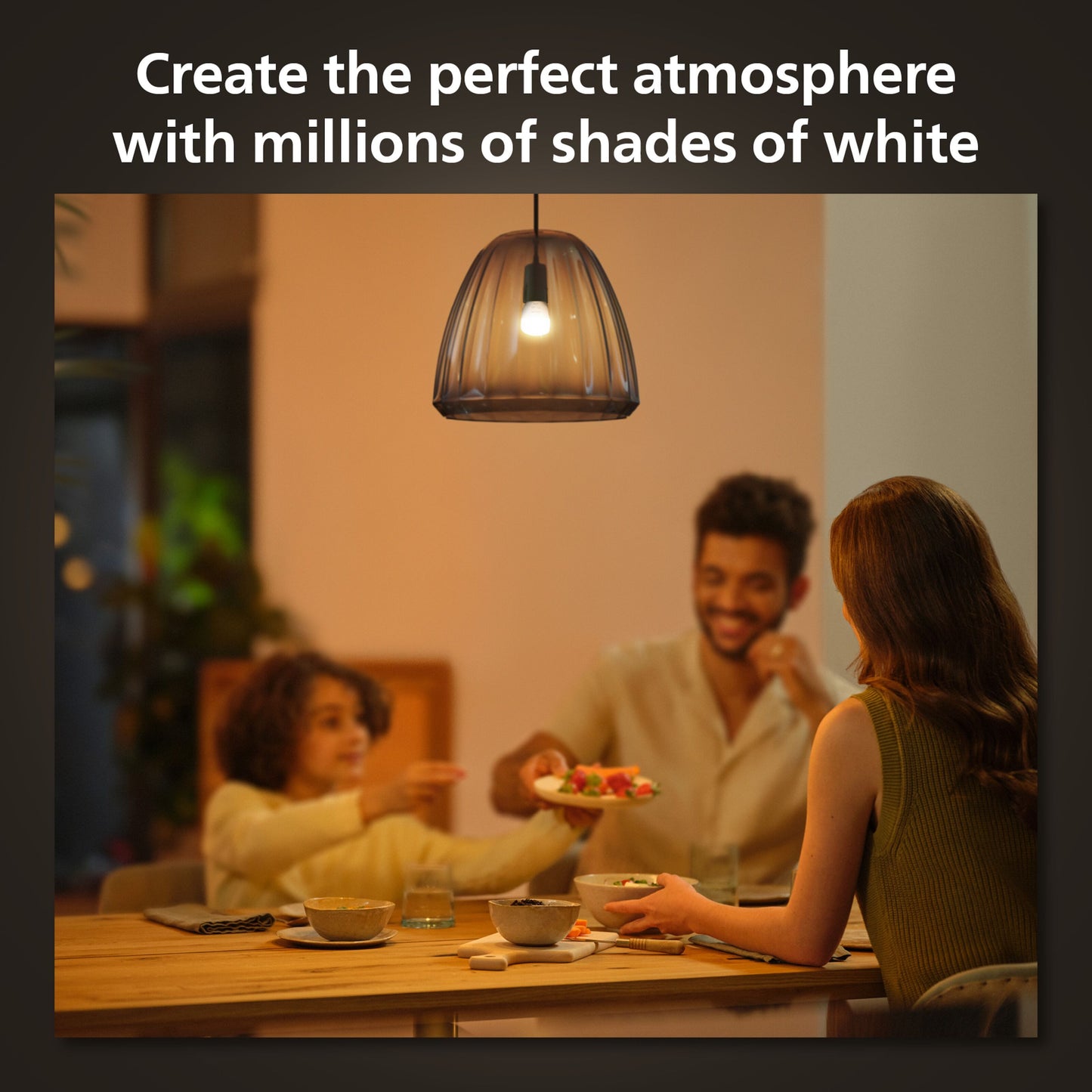 Hue Luster Kuglelampe White Ambiance E14 470 lm over spisebord, synlige personer under lampen, tekst: Skab den perfekte atmosfære.
