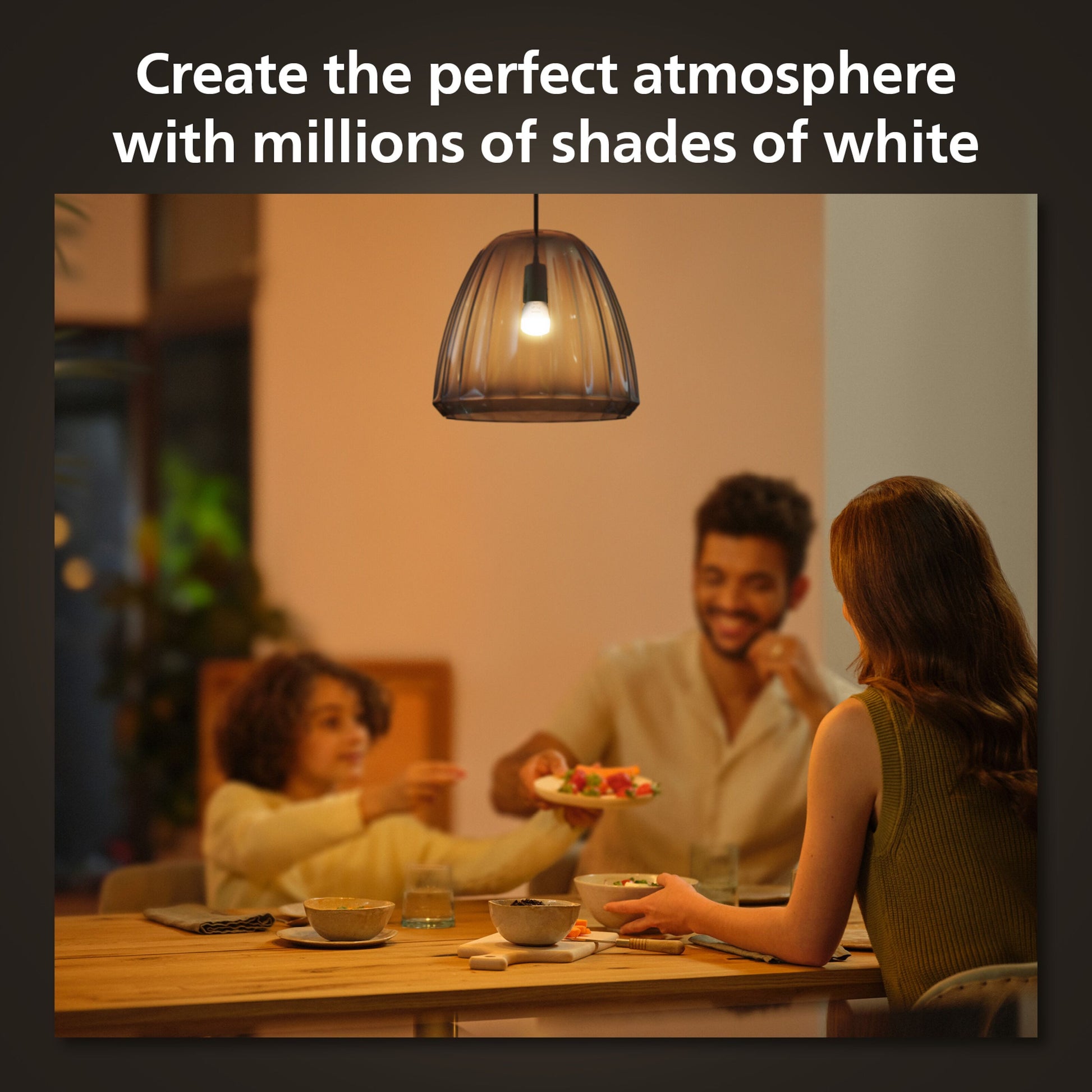 Hue Luster Kuglelampe White Ambiance E14 470 lm over spisebord, synlige personer under lampen, tekst: Skab den perfekte atmosfære.