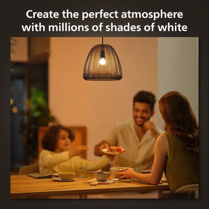 Hue Luster Kuglelampe White Ambiance E14 470 lm over spisebord, synlige personer under lampen, tekst: Skab den perfekte atmosfære.