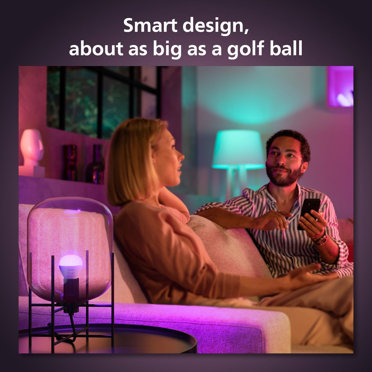 Philips Hue Luster Kuglelampe White and Color Ambiance E14 470 lm ved sofa, tekst: Smart design, omtrent så stor som en golfbold.
