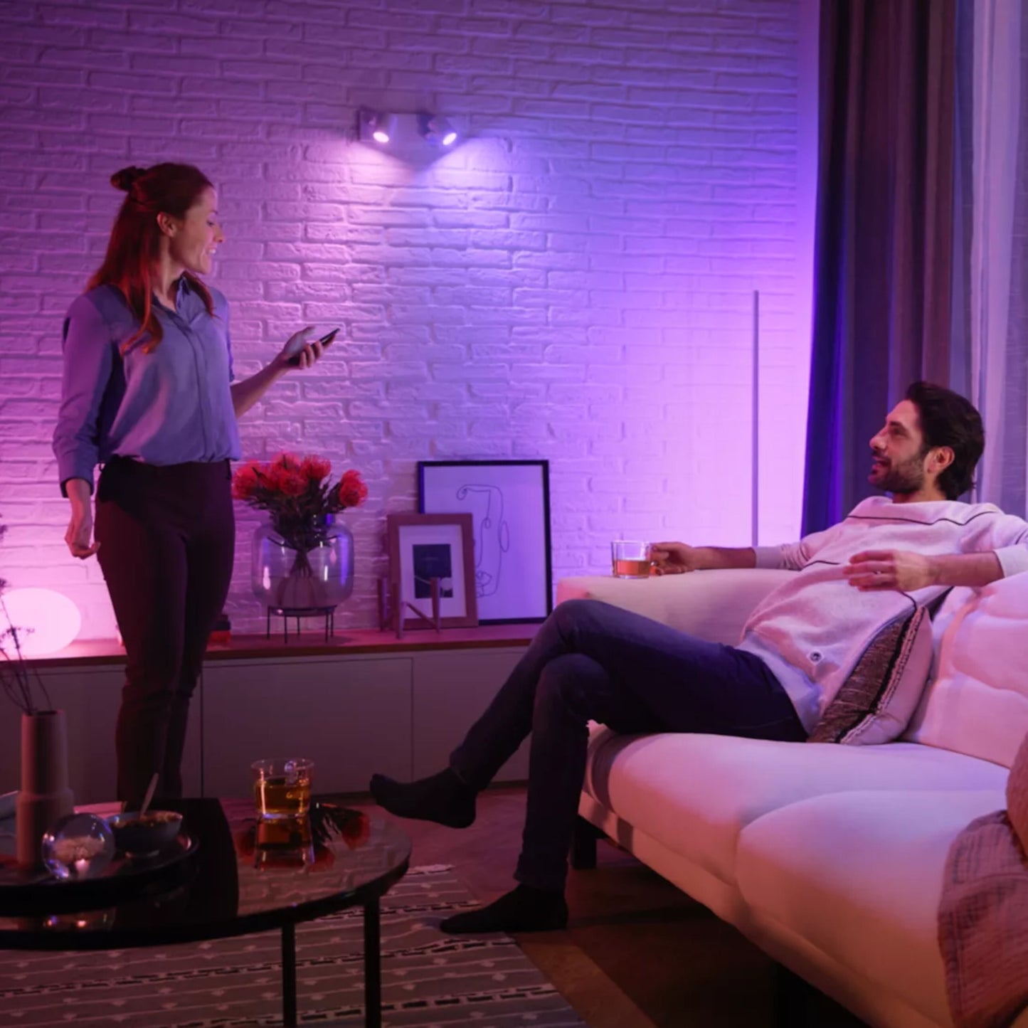 Philips Hue Hvid og Farveambiance MR16 400 lm smart belysning lyser rummet pink/lilla, synlig sofa og telefon.