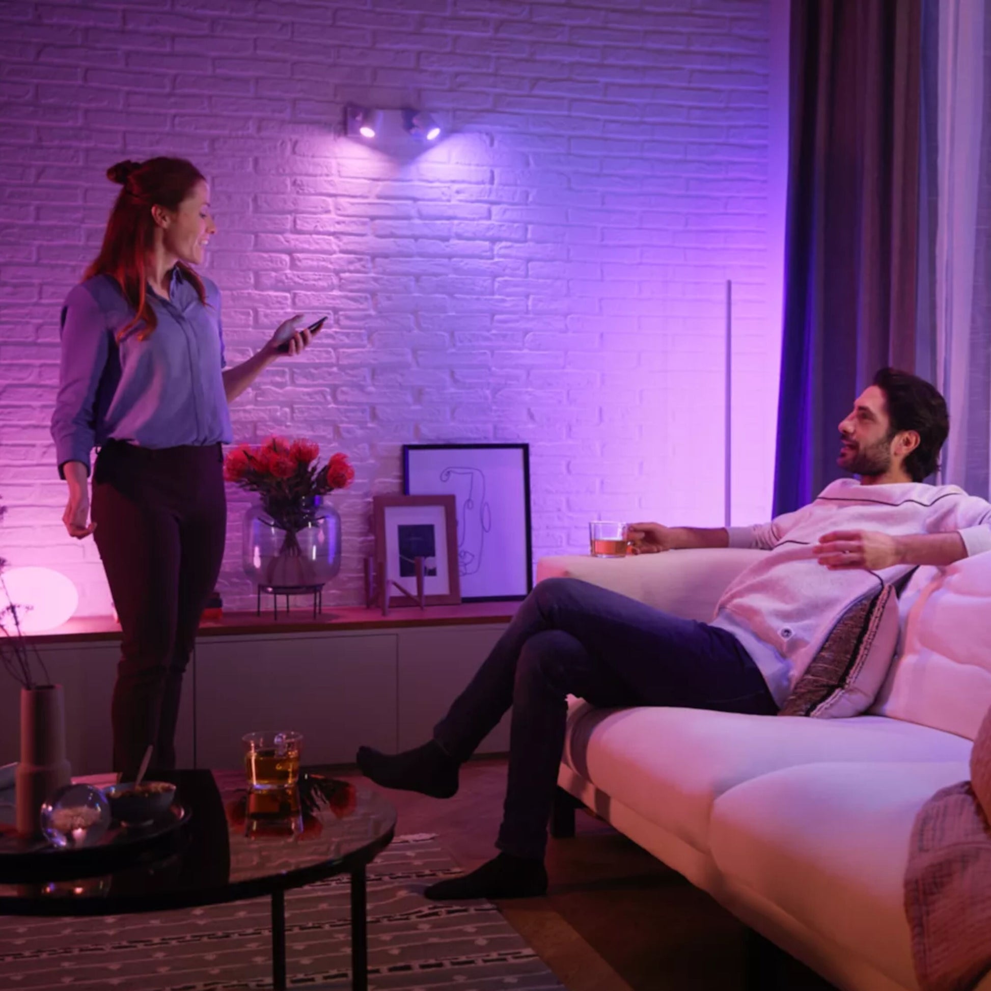 Philips Hue Hvid og Farveambiance MR16 400 lm smart belysning lyser rummet pink/lilla, synlig sofa og telefon.
