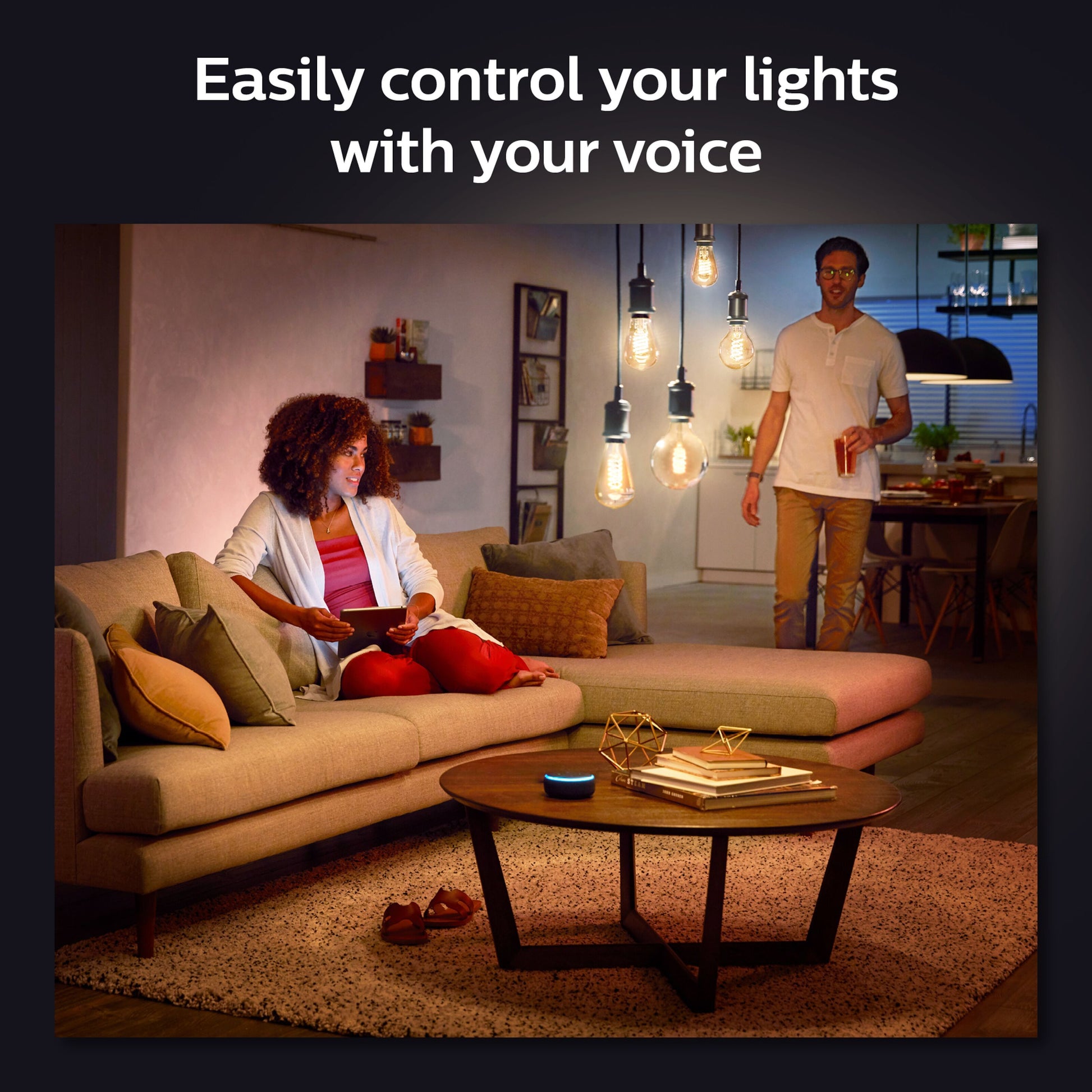 Philips Hue Filament G93 E27 Smart LED-pære 550 lm i loftet, smarte højtalere på sofabord, tekst: Styr nemt dine lys.