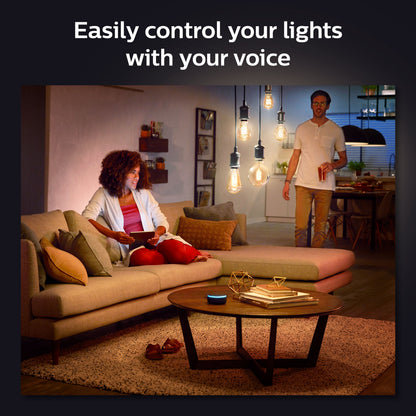 Philips Hue Filament G93 E27 Smart LED-pære 550 lm i loftet, smarte højtalere på sofabord, tekst: Styr nemt dine lys.