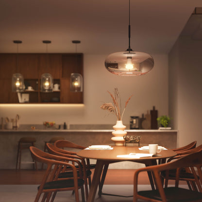 Hue Color Ambiance Smart LED-pære E27 1600 lm i pendel over rundt spisebord med fem stole og hvid vase med tørrede græsser.