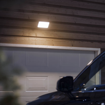 Philips Hue Udendørs Opdag projektør 2250 lm monteret over lukket garageport på træfacade, mørk bil foran.