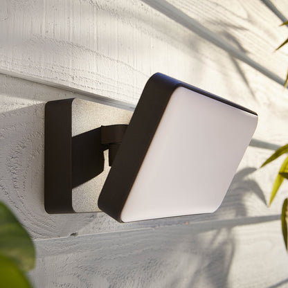 Philips Hue Opdag Udendørs projektør 2250 lm, matteret panel, mørk ramme, monteret på hvid trævæg med grønt blad.