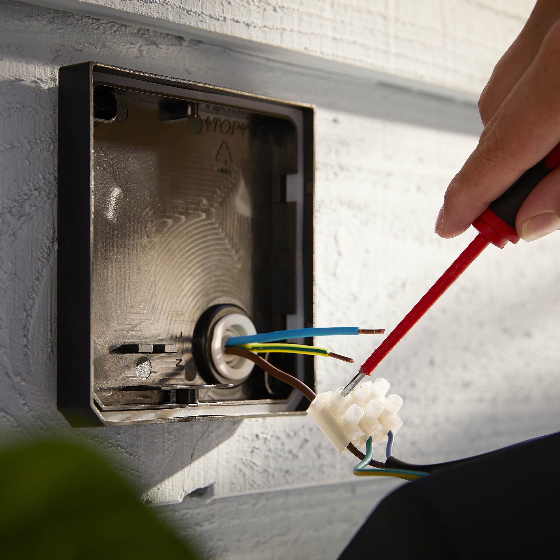Philips Hue Opdag Udendørs projektør 2250 lm, tilslutning af ledninger i vægboks med rød skruetrækker på lys ydervæg.