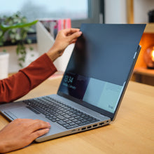 Trust Privatlivsfilter til 15,6" bærbar monteres på laptop ved træskrivebord, hånd på filter og tastatur.