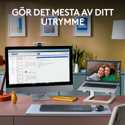 Logitech MK950 Signature Slim trådløst tastatur og mus på skrivebord med skærm, bakke og laptop på stativ.