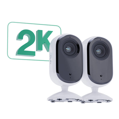 Arlo Essential 2K indendørskameraer side om side på stativer med grøn 2K videoopløsning og bevægelsesregistrering grafik.