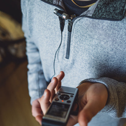 Om System WS-882 diktafon i hånd, lille mikrofon klipset på grå lynlåsjakke, synlig stereo-optagelse.