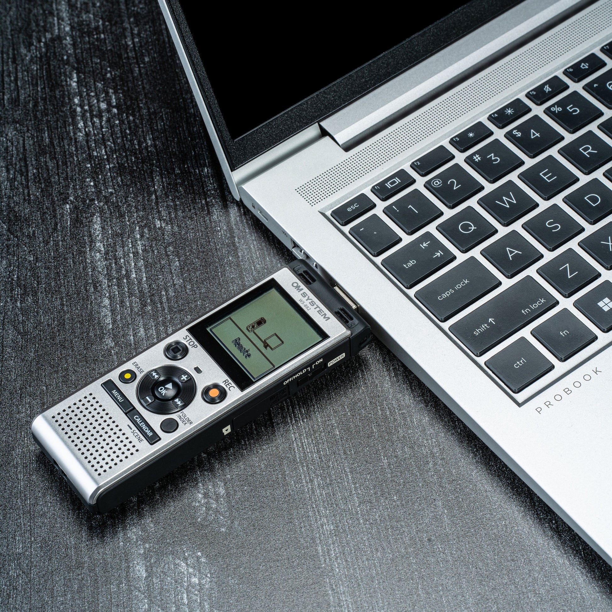 Om System WS-882 diktafon tilsluttet sølvfarvet laptop via USB, PC Link på display, del af tastatur synlig.