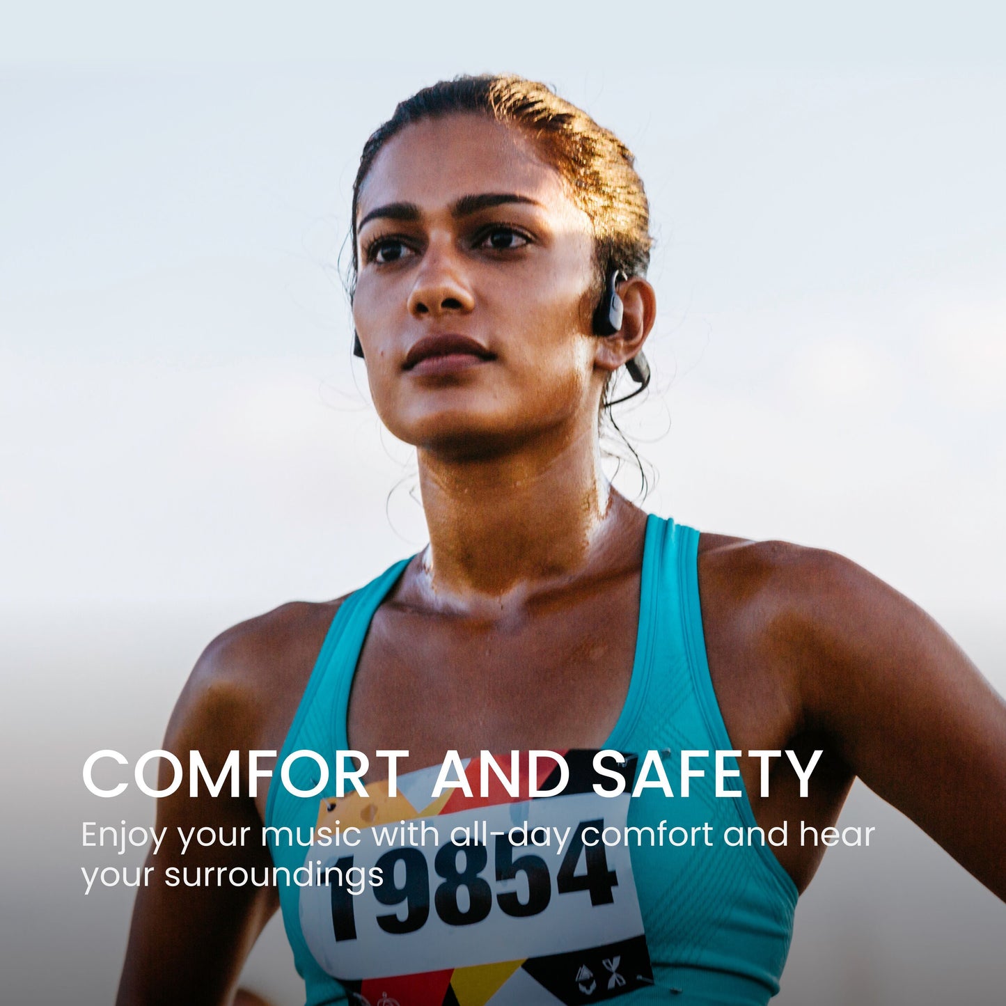 Shokz OpenRun Mini trådløse øretelefoner USB-C på kvindelig løber med startnummer, tekst: Komfort og sikkerhed.