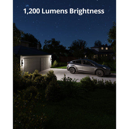 Eufy Væglampe med kamera S100 belyser indkørsel og garage, 1.200 lumen, sølv bil synlig, omgivet af træer/buske.