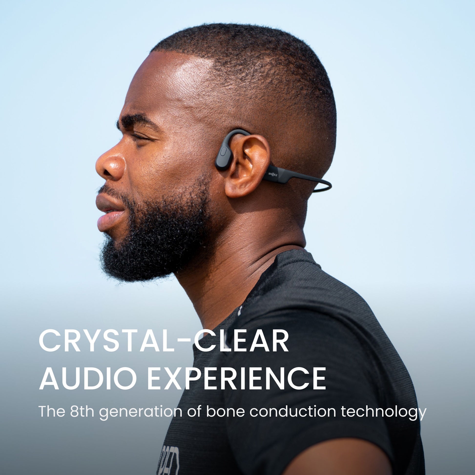 Shokz OpenRun trådløse hovedtelefoner USB-C, sort, 8. gen bone conduction, bæres af mand, blå himmel baggrund.