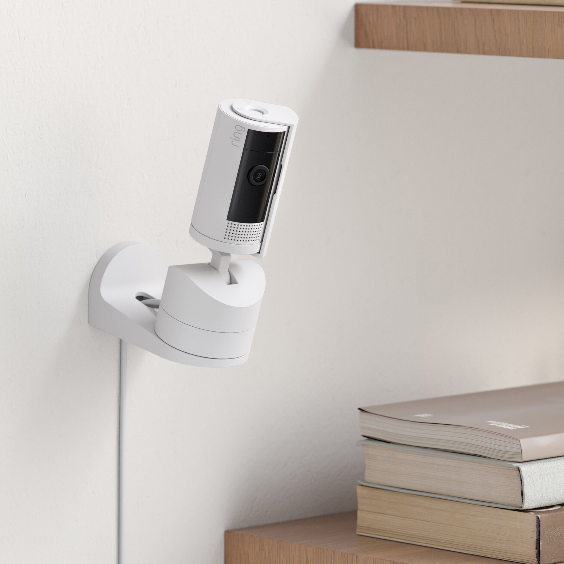 Ring Pan-Tilt indendørs kamera hvid monteret på væg ved træhylder med bøger, farve-nattesyn, synligt kabel.