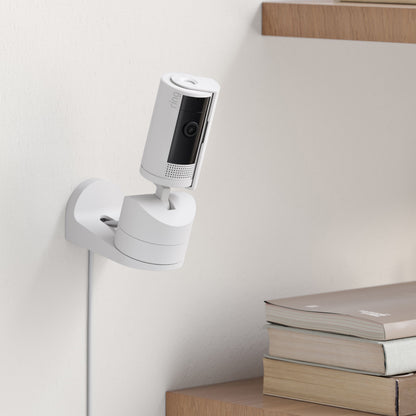 Ring Pan-Tilt indendørs kamera hvid monteret på væg ved træhylder med bøger, farve-nattesyn, synligt kabel.