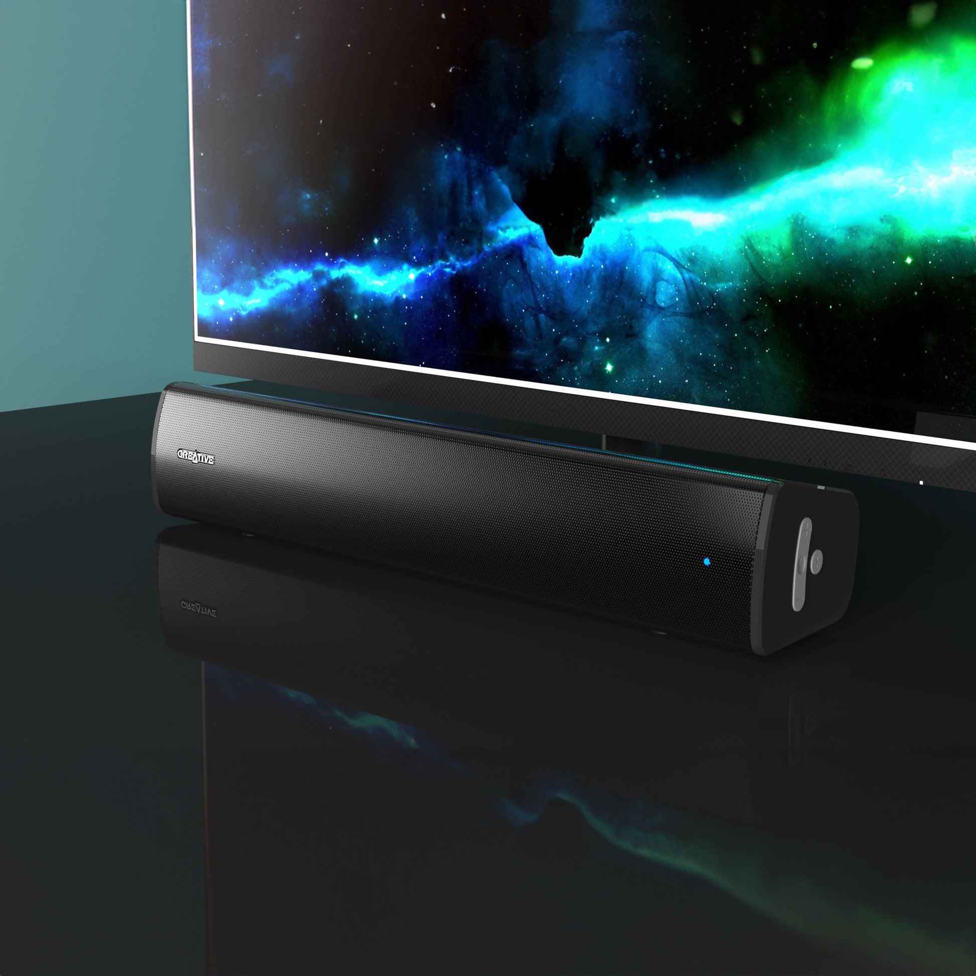 Creative Scene Air V2 sort Bluetooth soundbar med blå indikatorlys på blank sort overflade under tv med rum-motiv.