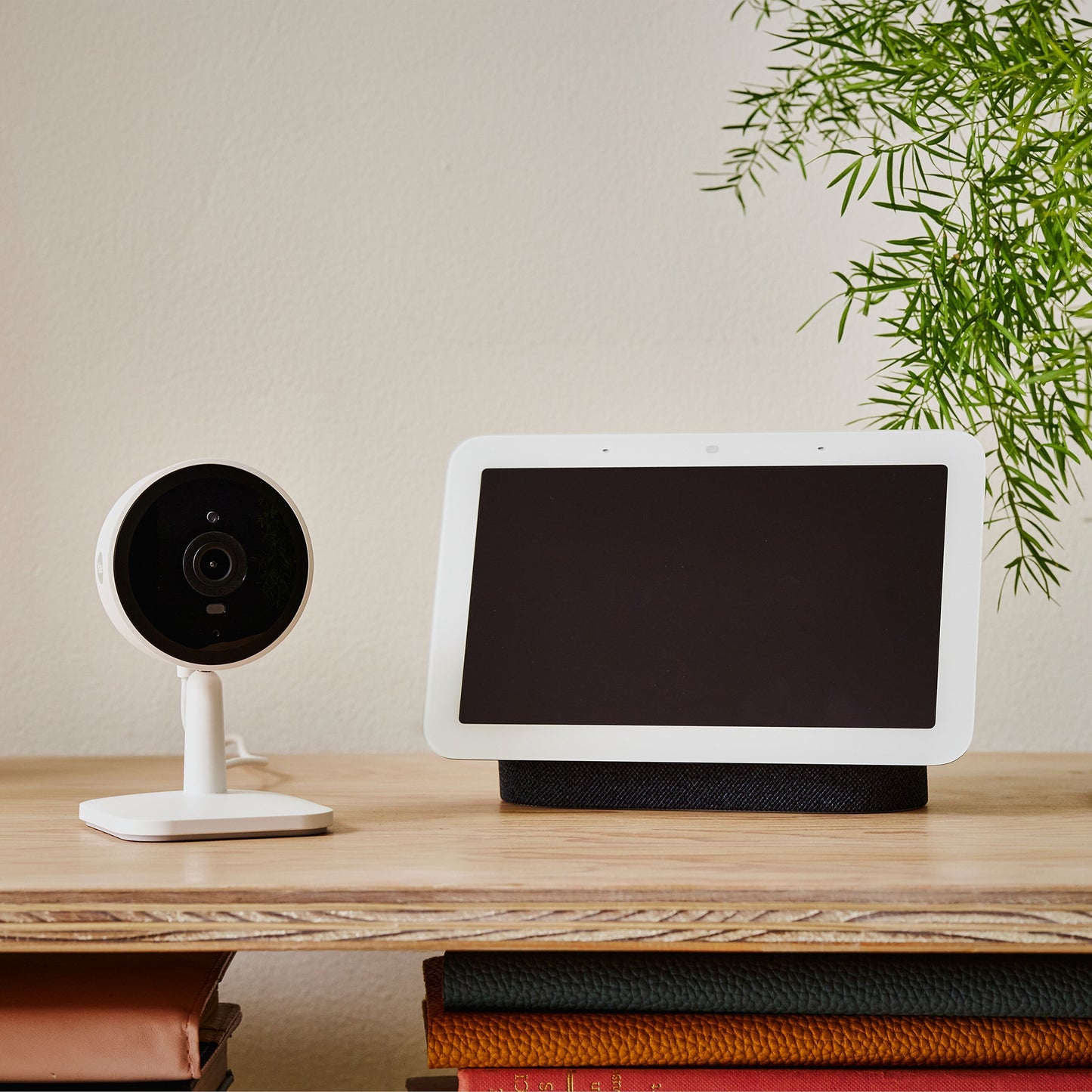Yale Smart indendørskamera på træhylde ved siden af smart display med blank skærm, bøger og grøn plante.