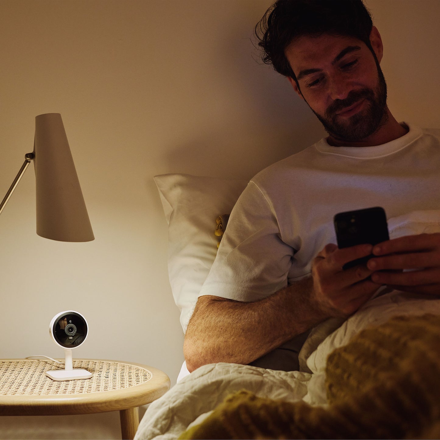 Yale Smart indendørskamera sorterer sæt fra siden på natbord ved seng, synlig linse og LED-lampe.