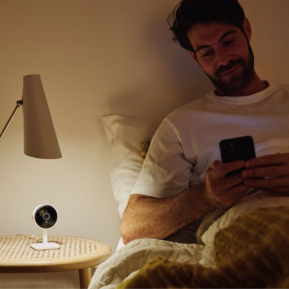 Yale Smart indendørskamera sorterer sæt fra siden på natbord ved seng, synlig linse og LED-lampe.
