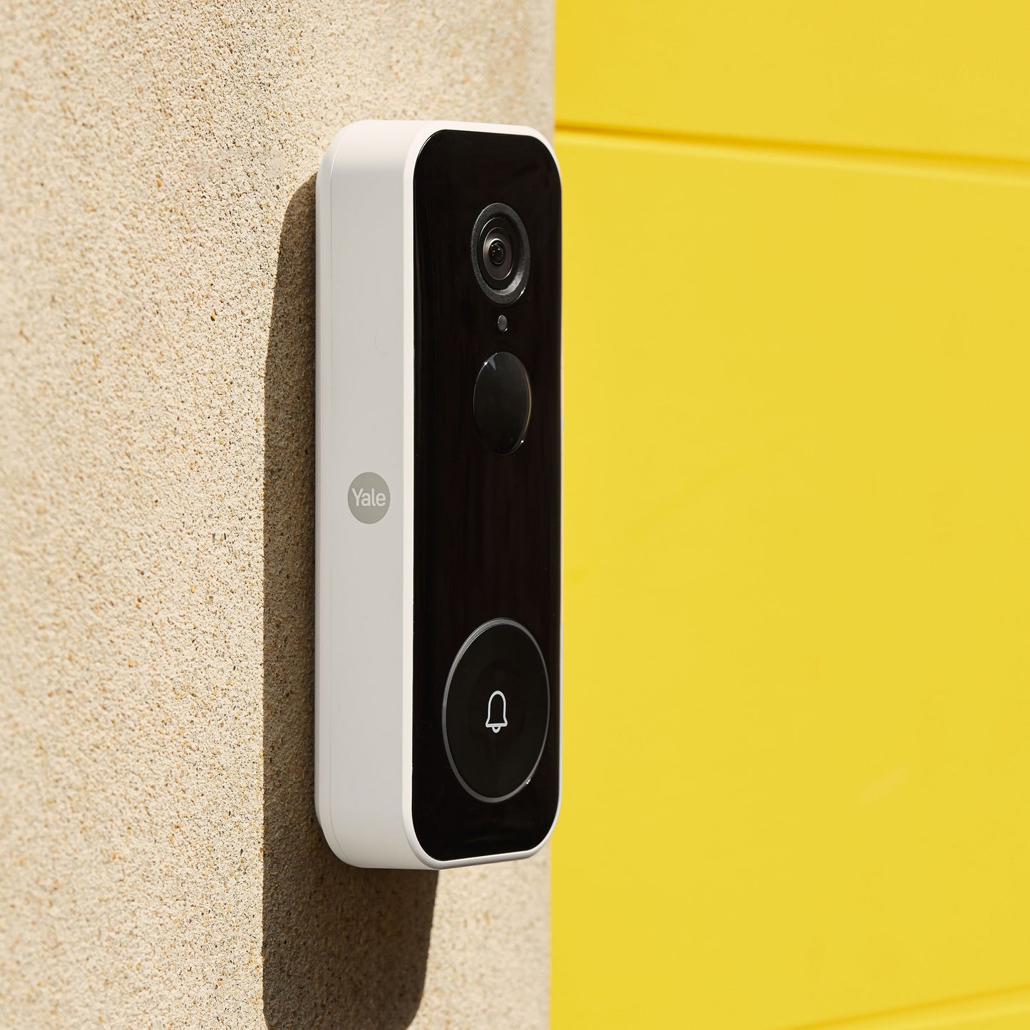 Yale Smart video dørklokke sort frontpanel hvide sider monteret på beige væg ved gul flade.
