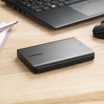 Toshiba Canvio Basics ekstern harddisk 4TB sort med blå indikatorlys ved siden af laptop og mus.