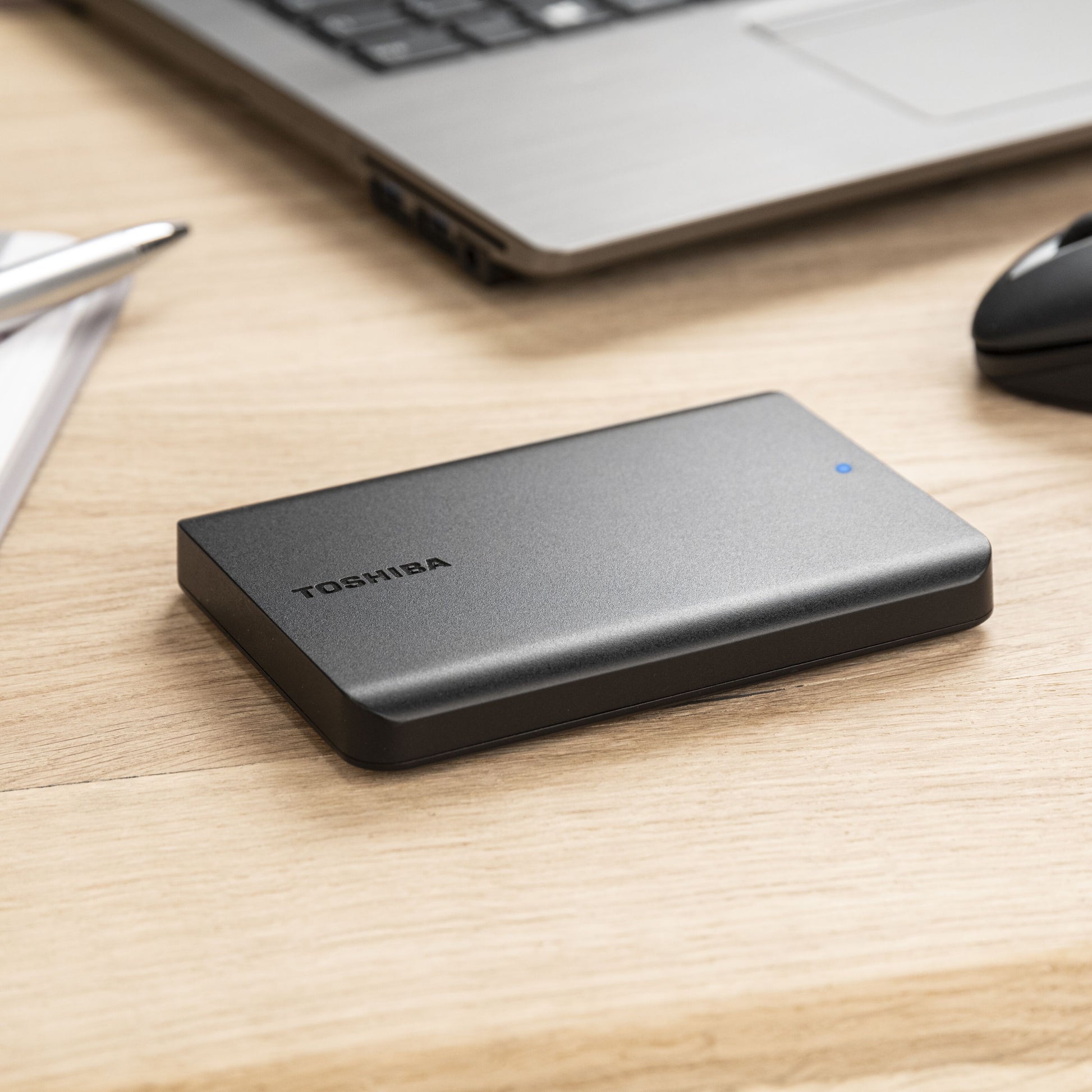 Toshiba Canvio Basics ekstern harddisk 4 TB sorteret ved siden af laptop, mus og papirer på træskrivebord.